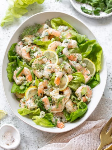 A platter of shrimp salad with layers of butter lettuce, shrimp, herbs and lemon slices.