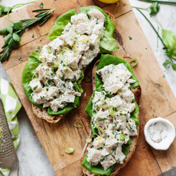 Chicken salad sandwiches served open-face on a wooden cutting board.
