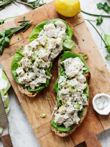 Chicken salad sandwiches served open-face on a wooden cutting board.