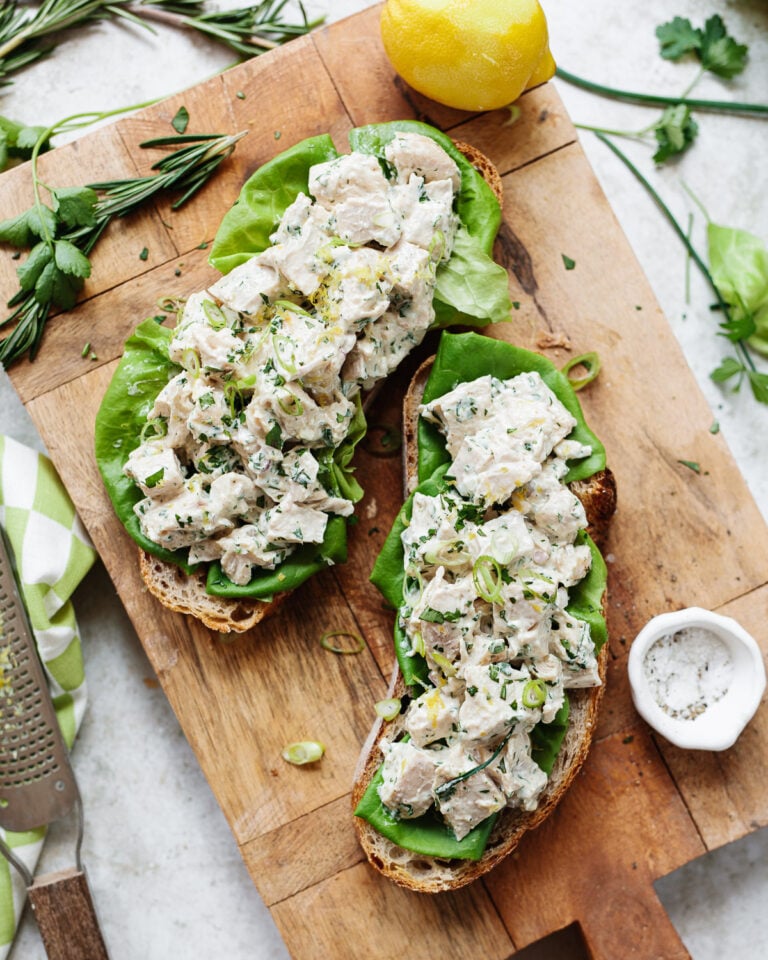 Chicken salad sandwiches served open-face on a wooden cutting board.