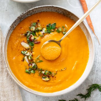 Creamy carrot soup in a serving bowl, with chopped almonds and parsley garnished on top and a spoon.