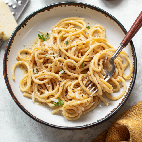 Cacio e pepe pasta in a serving bowl, with a fork resting on the side.