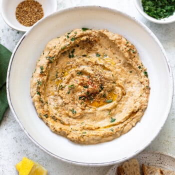 Creamy baba ganoush (eggplant dip) on a plate, with a swirl of olive oil, sesame seeds and chopped parsley on top.
