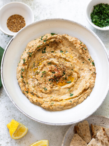 Creamy baba ganoush (eggplant dip) on a plate, with a swirl of olive oil, sesame seeds and chopped parsley on top.