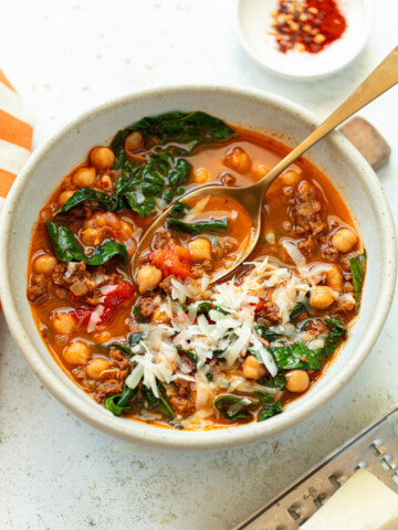 Chorizo chickpea stew garnished with shredded cheese in a serving bowl.