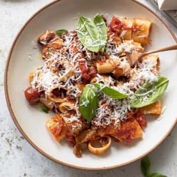 A serving of pasta alla Norma in a bowl, topped with fresh basil and grated cheese.
