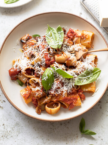 Pasta alla Norma in a serving bowl, topped with fresh basil and grated fresh cheese.