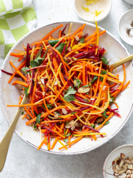 Matchstick-cut fresh carrot salad in a bowl, with serving utensils set alongside.