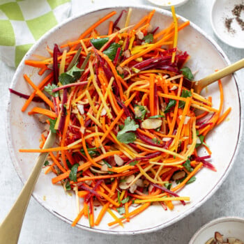 Matchstick-cut fresh carrot salad in a bowl, with serving utensils set alongside.