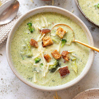A serving of cheddar and broccoli soup in a bowl, with a spoon resting on the side.
