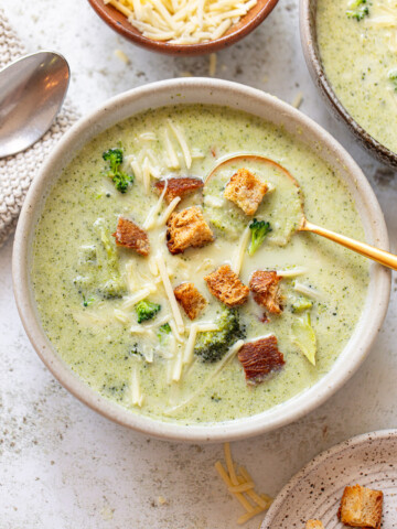 A serving of cheddar and broccoli soup in a bowl, with a spoon resting on the side.