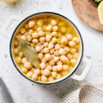 Cooked chickpeas (garbanzo beans) in a pot of water, with a bay leaf on top.