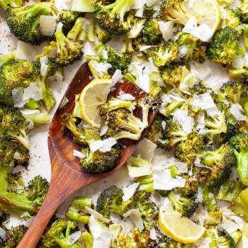 Roasted broccoli with grated Parmesan cheese and lemon slices on a sheet pan, with a wooden spatula resting on the side.