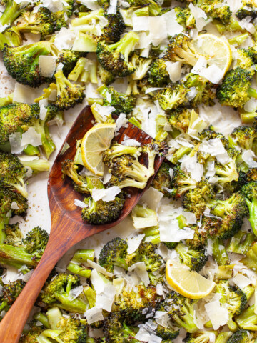 Roasted broccoli with grated Parmesan cheese and lemon slices on a sheet pan, with a wooden spatula resting on the side.