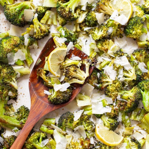 Roasted broccoli with grated Parmesan cheese and lemon slices on a sheet pan, with a wooden spatula resting on the side.
