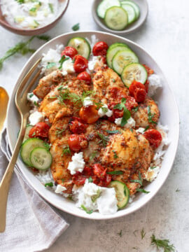 Chicken souvlaki-style, on a platter over rice with tzatziki sauce and roasted tomatoes.