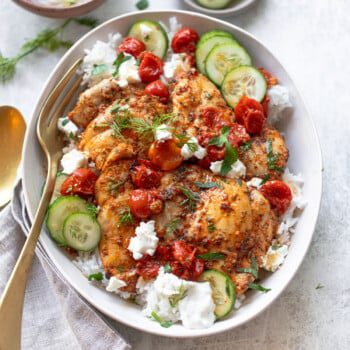 Chicken souvlaki-style, on a platter over rice with tzatziki sauce and roasted tomatoes.