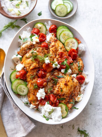 Chicken souvlaki-style, on a platter over rice with tzatziki sauce and roasted tomatoes.
