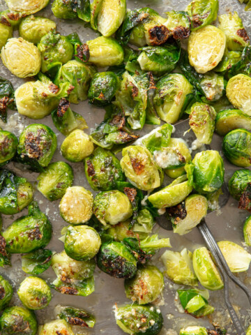 Roasted Brussels sprouts on a sheet pan, with crisp brown edges and melted Parmesan cheese.