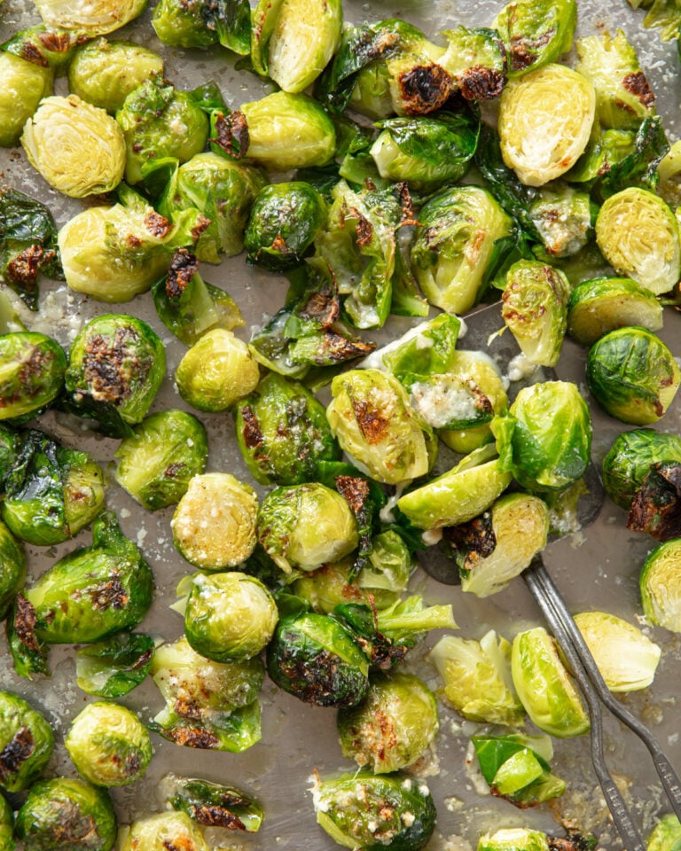 Roasted Brussels sprouts on a sheet pan, with crisp brown edges and melted Parmesan cheese.