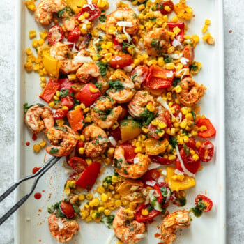 Baked spicy shrimp on a sheet pan with roasted corn, tomatoes and chopped bell peppers.