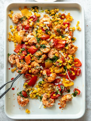 Baked spicy shrimp on a sheet pan with roasted corn, tomatoes and chopped bell peppers.