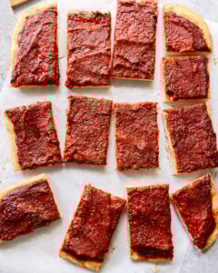 Rectangular slices of pizza with a thick layer of tomato sauce and herbs on top, arranged on parchment paper. The pizza has no visible cheese or other toppings.