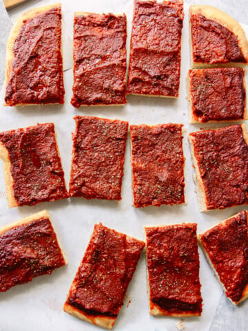 Rectangular slices of pizza with a thick layer of tomato sauce and herbs on top, arranged on parchment paper. The pizza has no visible cheese or other toppings.