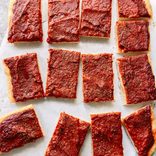 Rectangular slices of pizza with a thick layer of tomato sauce and herbs on top, arranged on parchment paper. The pizza has no visible cheese or other toppings.
