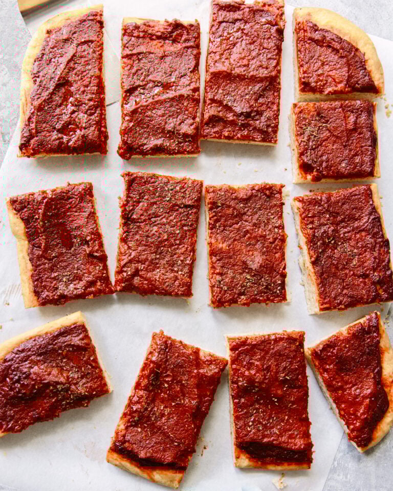 Rectangular slices of pizza with a thick layer of tomato sauce and herbs on top, arranged on parchment paper. The pizza has no visible cheese or other toppings.