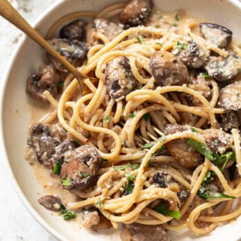 A bowl of linguine with creamy sauce, sautéed mushrooms, grated parmesan, and fresh herbs, with a fork twirled into the pasta.