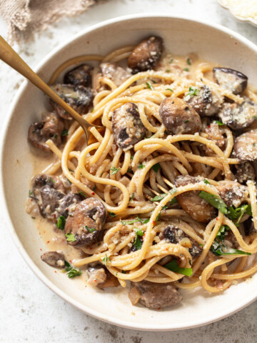 A bowl of linguine with creamy sauce, sautéed mushrooms, grated parmesan, and fresh herbs, with a fork twirled into the pasta.