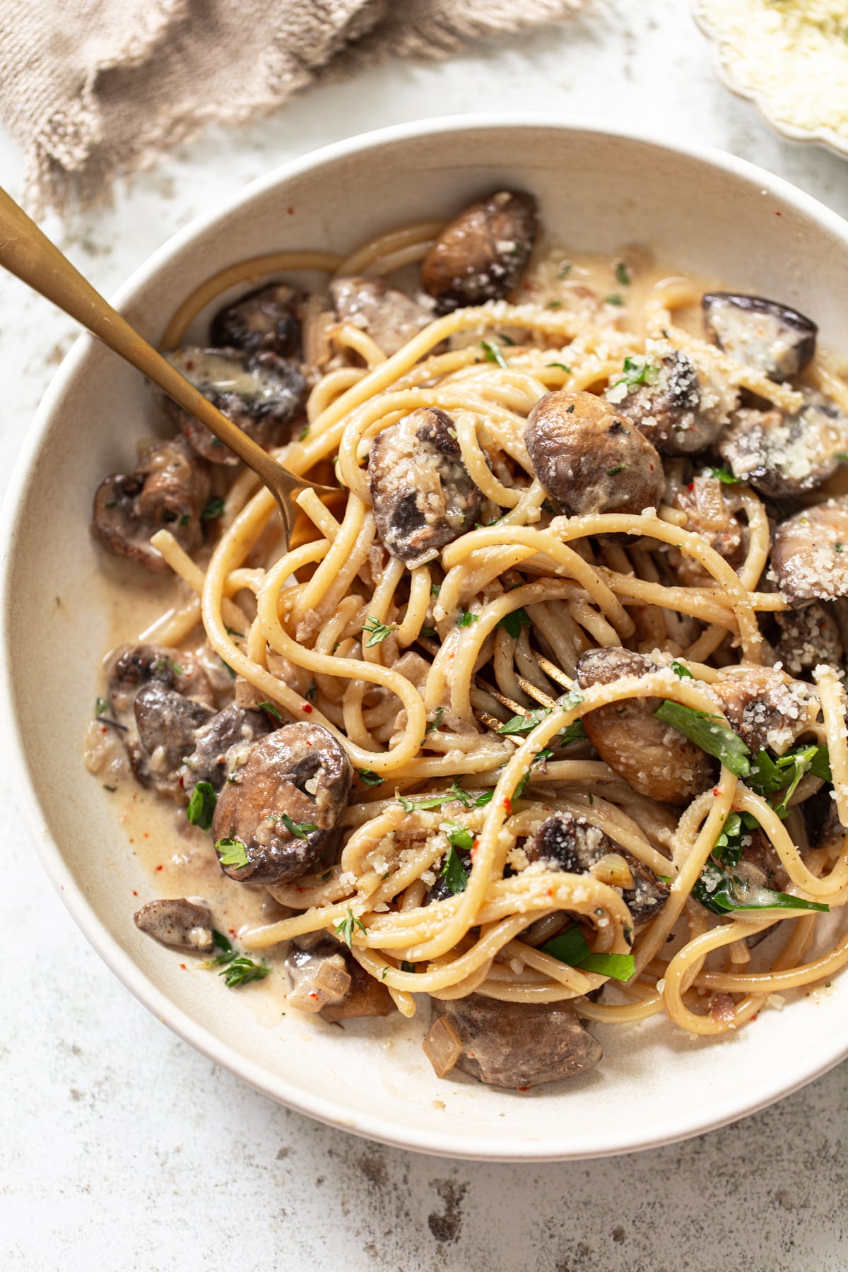 A bowl of linguine with creamy sauce, sautéed mushrooms, grated parmesan, and fresh herbs, with a fork twirled into the pasta.